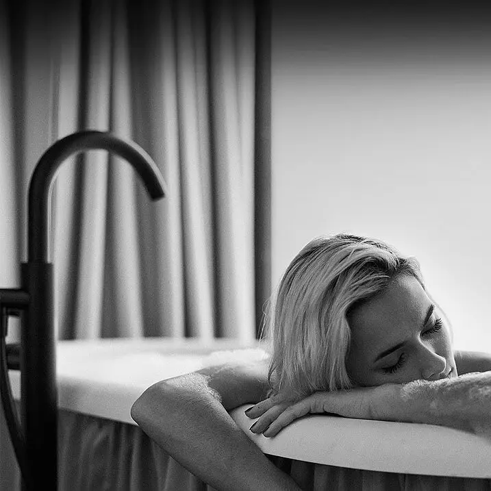 A woman in a bathtub leans on the edge and relaxes.