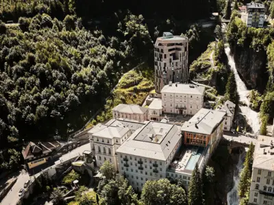 Luftaufnahme des historischen Kurortes Bad Gastein mit modernen und klassischen Hotelbauten, Wasserfall und grüner Berglandschaft im Sommer.
