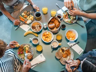 Top-down view of a round breakfast table with four people enjoying rolls, fruit and shared dishes at Urban Nature.