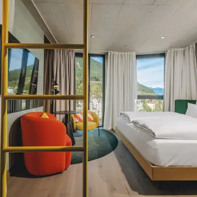 Helles Designhotel-Zimmer mit Panoramafenstern, moderner Einrichtung, bunten Sesseln und Blick auf die Bergwelt von Bad Gastein