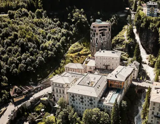Luftaufnahme des historischen Kurortes Bad Gastein mit modernen und klassischen Hotelbauten, Wasserfall und grüner Berglandschaft im Sommer.