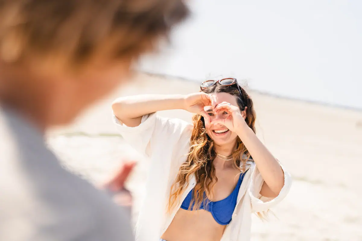 A woman in a bikini is forming a heart shape with her hands.