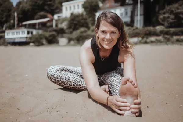 A woman is stretching her leg on the beach.
