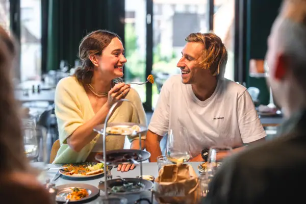 Auntie Clara Gäste Eine Frau hebt eine Gabel an den Mund eines Mannes in einem Restaurant.