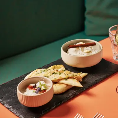 An appetizer with bread and dips is served on a slate board.