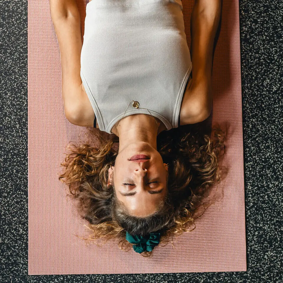 A woman is lying on a yoga mat with her eyes closed.