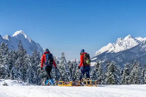 Zwei Menschen wandert auf einem verschneiten Berg und ziehen Schlitten hinter sich her.