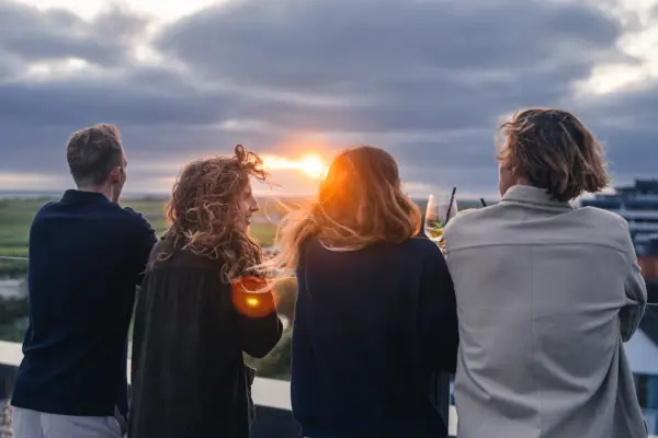 A group of people are standing on the rooftop bar Scraper's Club St. Peter-Ording watching the sunset.
