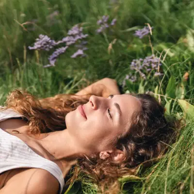 A woman lies in the grass with her eyes closed and smiles.