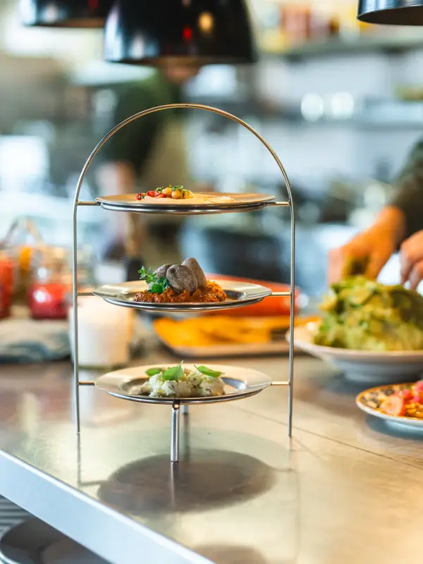 A tiered serving dish with three dips stands on a kitchen worktop, and a chef is working in the background.