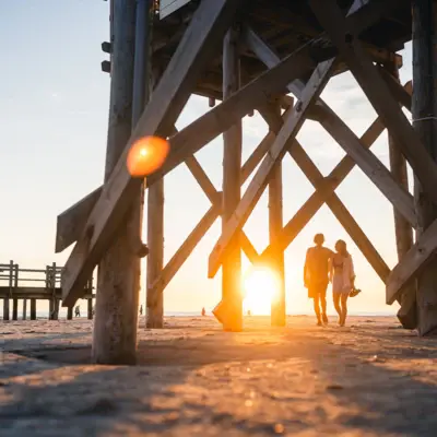 Couple walking arm in arm at sunset along St. Peter-Ording beach between the stilt houses.