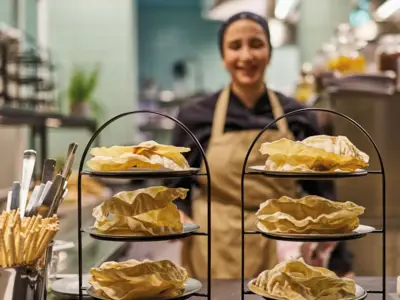 Two tiered trays stand in a kitchen and a cook stands behind them wearing an apron.