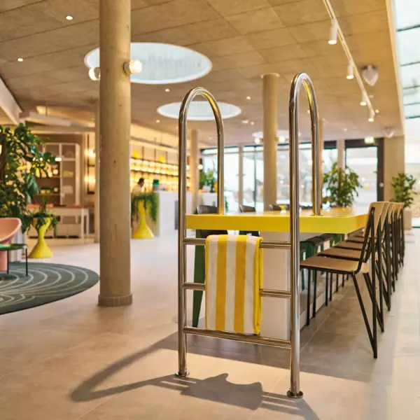 Kreatives Interior im Hotel:Modern gestalteter Rezeptionsbereich mit Schwimmbadleiter als Designelement, gelb-weißen Akzenten und stilvollen Sitzgelegenheiten.