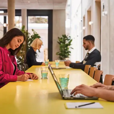 Meeting im Badeschloss Bad Gastein Co-Working-Bereich im Urban Nature Hotel Bad Gastein mit gelbem Tisch, Laptop, jungen Menschen beim Arbeiten und Schreiben