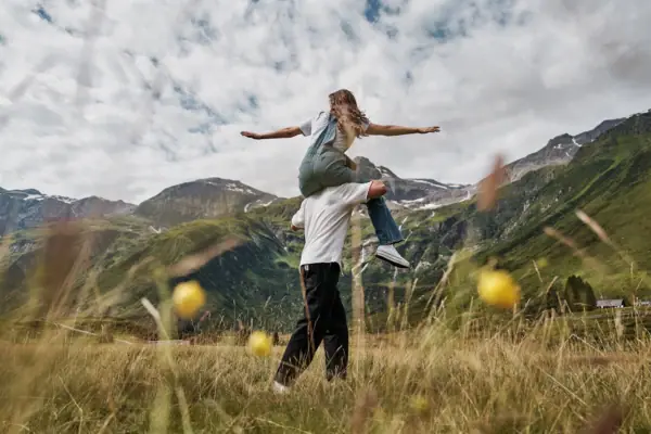 A man is carrying a woman on his shoulders in a grassy field.