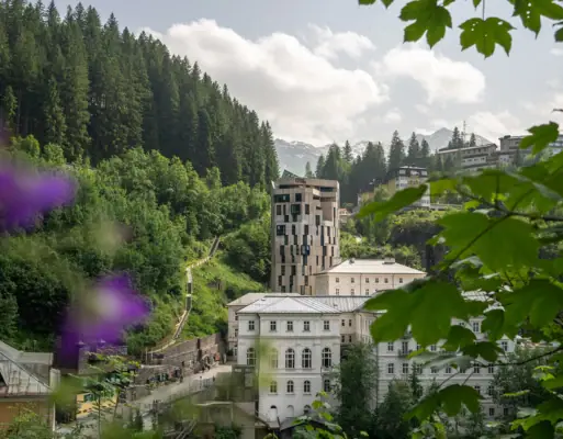 A group of buildings nestled within a lush forest under a partly cloudy sky.