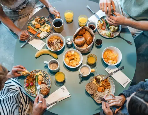Top-down view of a round breakfast table with four people enjoying rolls, fruit and shared dishes at Urban Nature.