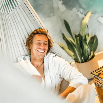 Guest in bathrobe lounging in a hammock, smiling.