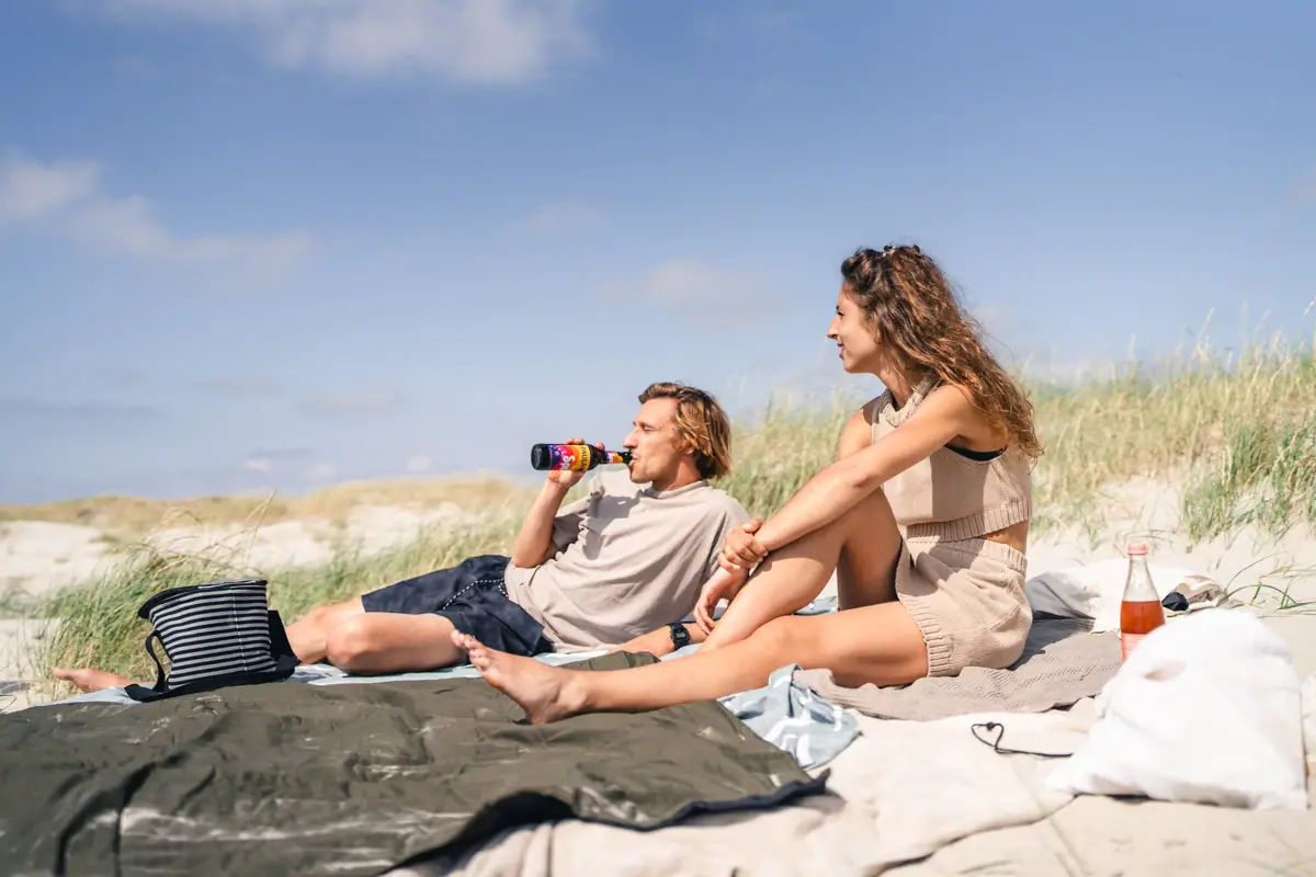 A man and a woman are sitting on a blanket on the beach.