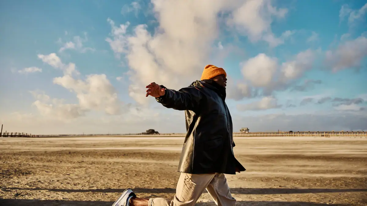 A man in a black coat and an orange cap on the sandy beach.