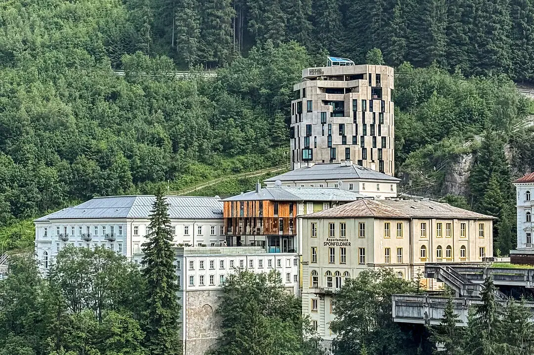 A building near a woodland, with trees and mountains in the background.