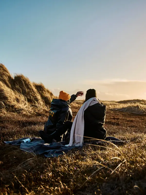 Two people are sitting on a blanket in a grassy area.