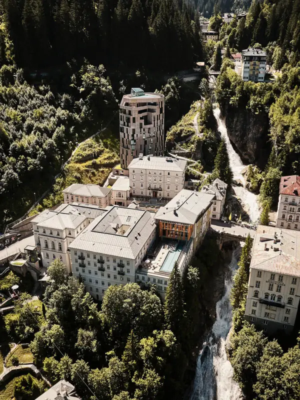 Luftaufnahme des Hotelensembles in Bad Gastein mit modernem Turm, historischen Gebäuden und Pool, eingebettet in grüne Berglandschaft