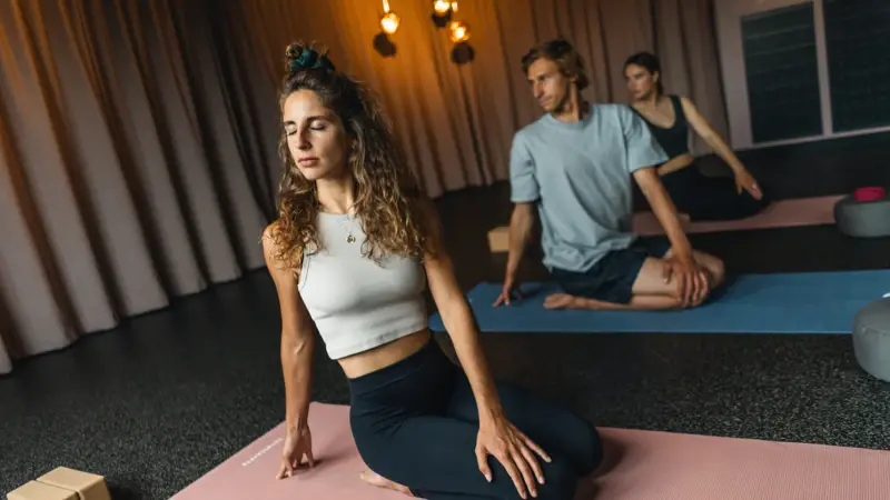 Three people relax while doing yoga on mats, keeping their eyes closed.