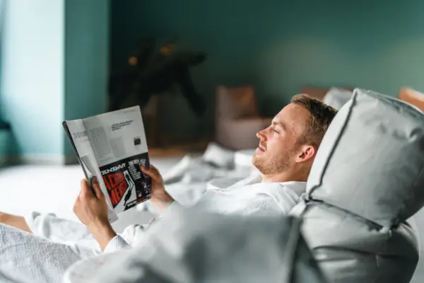 Ein Mann im Bademantel liegt auf einem gemütlichen Sitzsack und liest eine Zeitschrift.