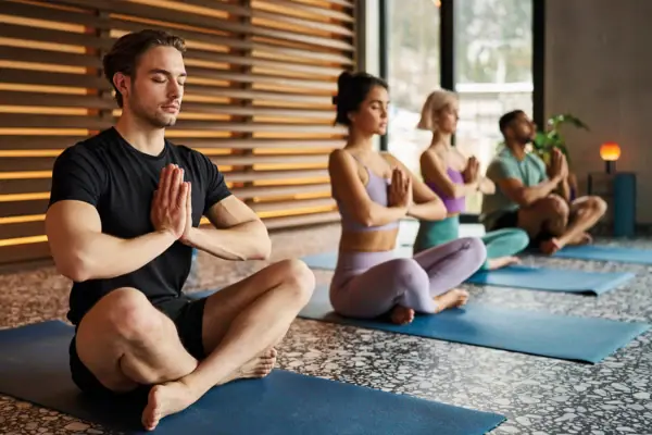 A group of people are sitting on yoga mats with their hands clasped.