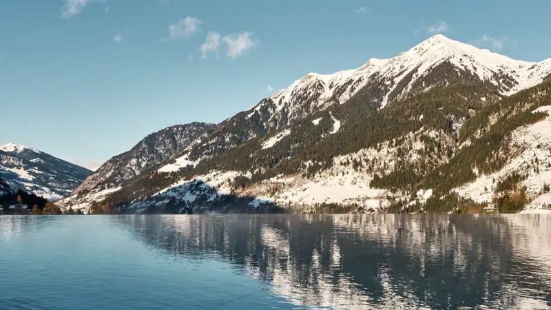 Mountains during winter A body of water with snow-covered mountains and a clear blue sky.