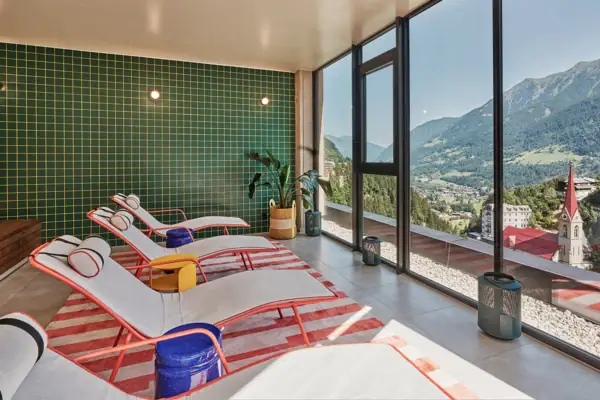 Ruheraum im Alpine Swim Club in Bad Gastein Moderner Ruheraum mit stylischen Liegen, großen Panoramafenstern und Blick auf die Berge und Kirche von Bad Gastein