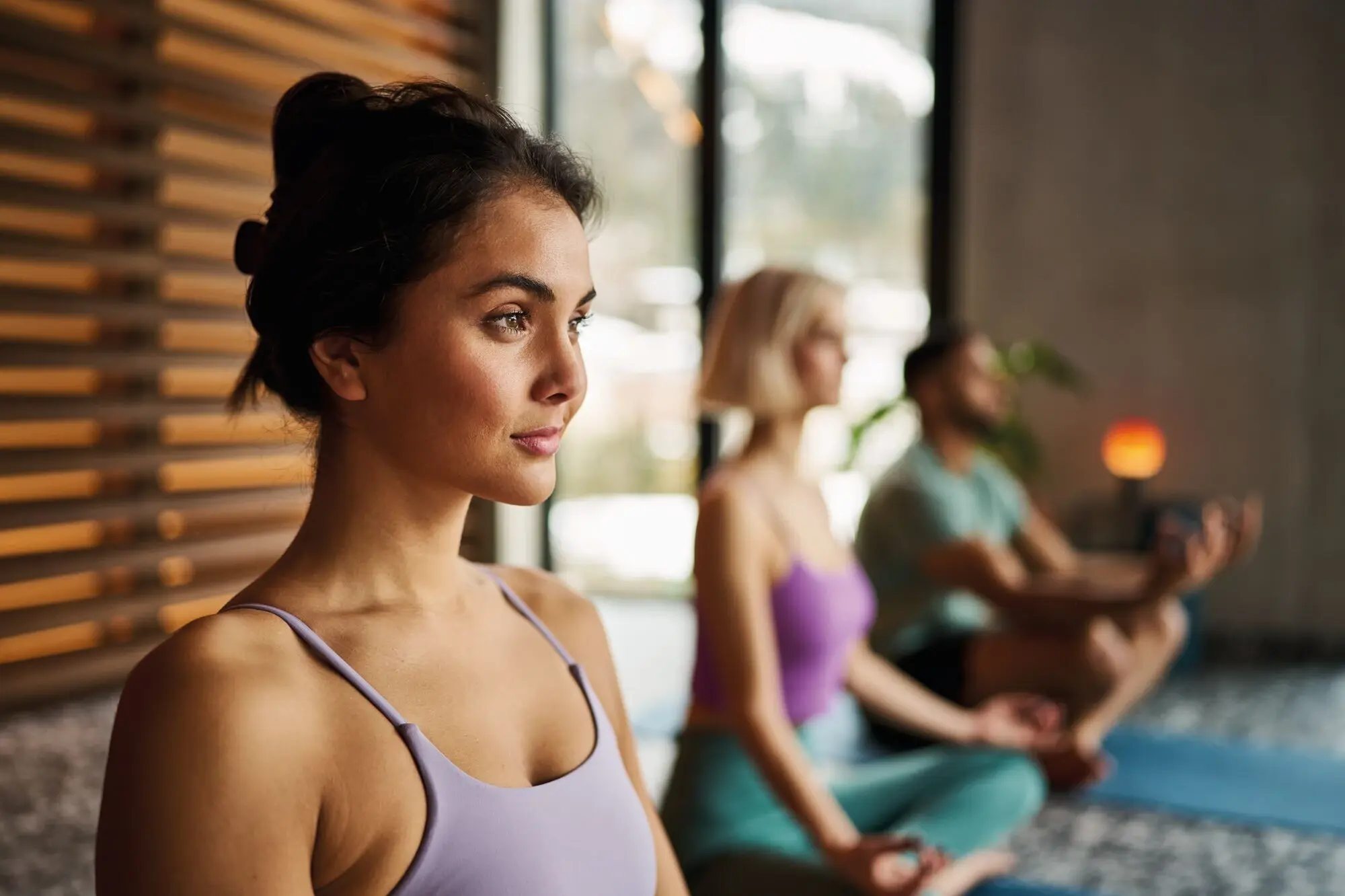 Yoga at the Alpine Swim Club Young woman in yoga pose with closed eyes, in the foreground of a meditation group in a modern, light-flooded room