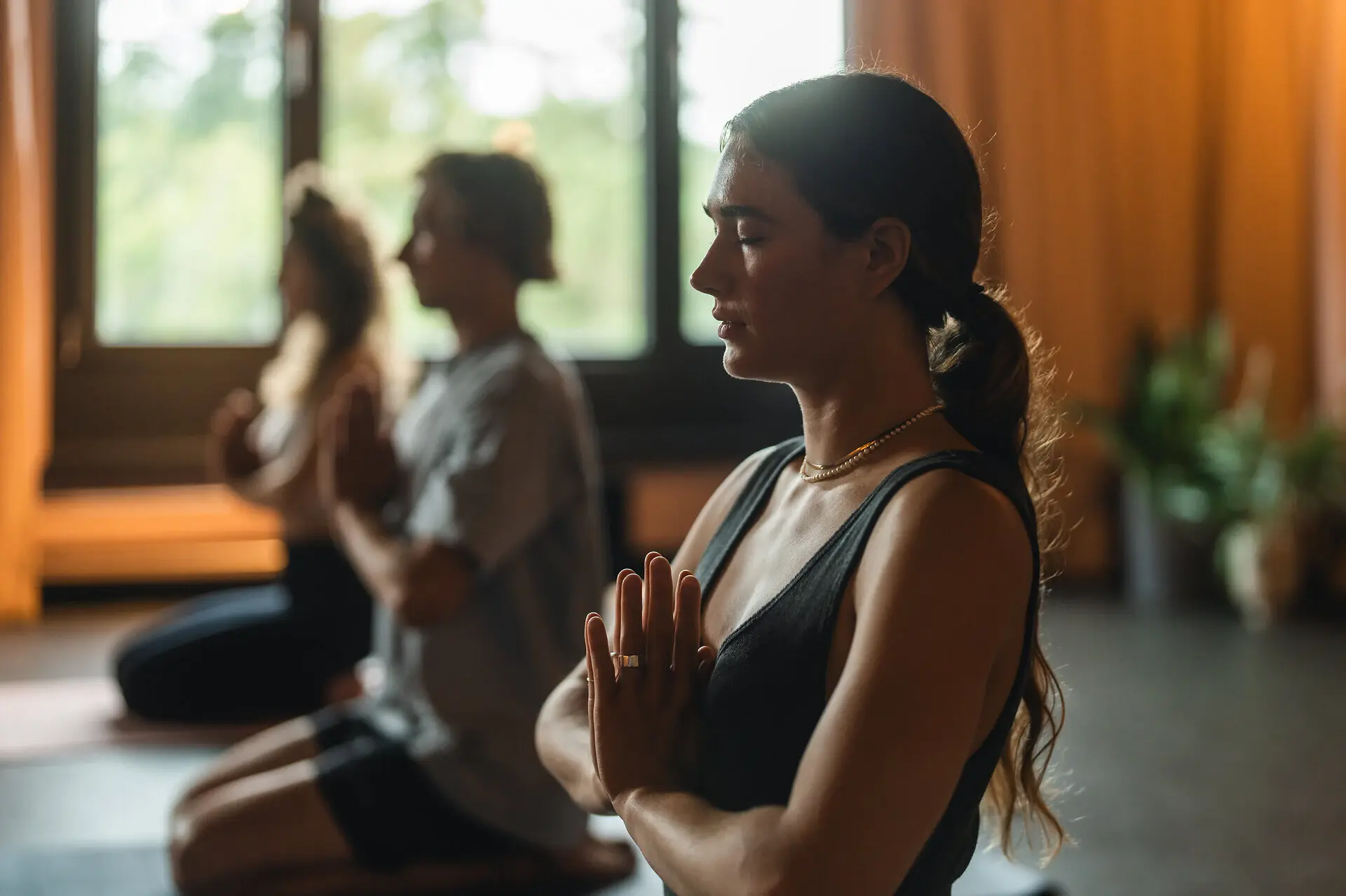 Yoga Urban Nature St. Peter-Ording Three people are sitting on a mat doing yoga and folding their hands in front of their chests.