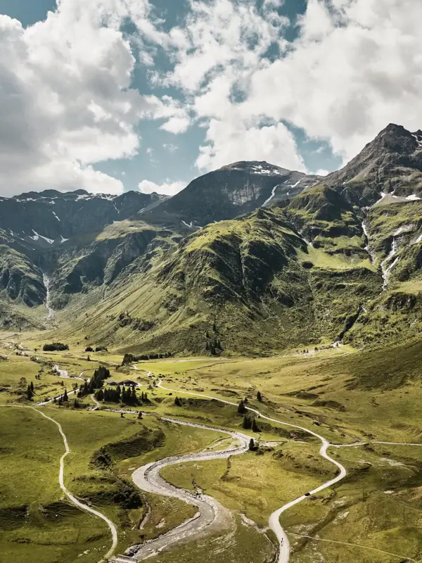 Weitläufige Alpenlandschaft mit grünen Berghängen, kurviger Straße und Bergfluss unter dramatischem Himmel – Naturidylle in der Region Bad Gastein