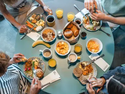 A round breakfast table photographed from above, with four people sitting around it eating bread rolls, fruit and other food.