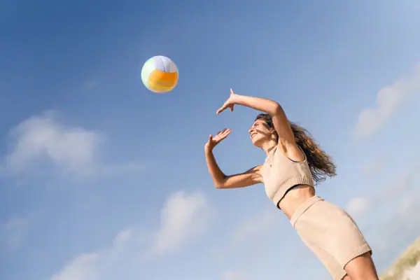 Eine Frau wirft eine. Beachvolleyball nach oben über ihrem Kopf und der blaue Himmel ist im Hintergrund zu sehen.