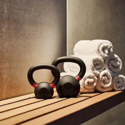 Two kettlebells and several rolled-up towels on a wooden bench in a modern fitness or wellness area