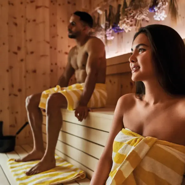 Man and woman taking a sauna in a modern wooden sauna with herbs with yellow and white striped towels