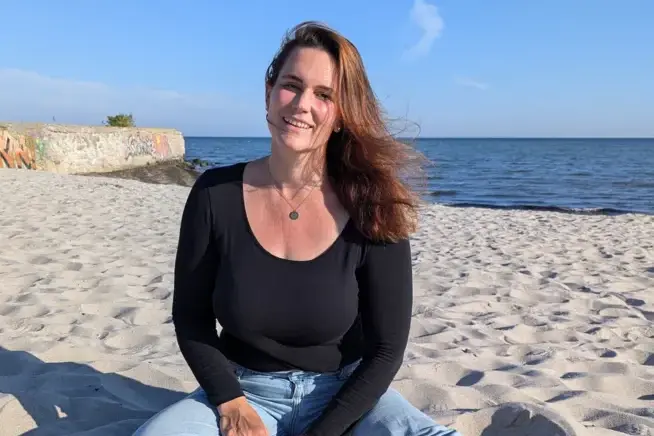 Yogalehrerin Ann-Katrin Feldkamp at the beach Yoga teacher Ann-Katrin Feldkamp sits cross-legged on the sand at the beach, with the sea visible in the background.