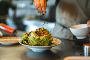 A person sprinkles greens on a plate of food.