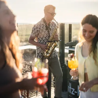 Saxophonist performing at Scraper’s Club rooftop bar with guests dancing and drinks in hand.