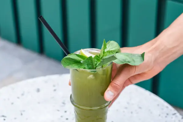 A hand places a green lemonade with basil on a table.
