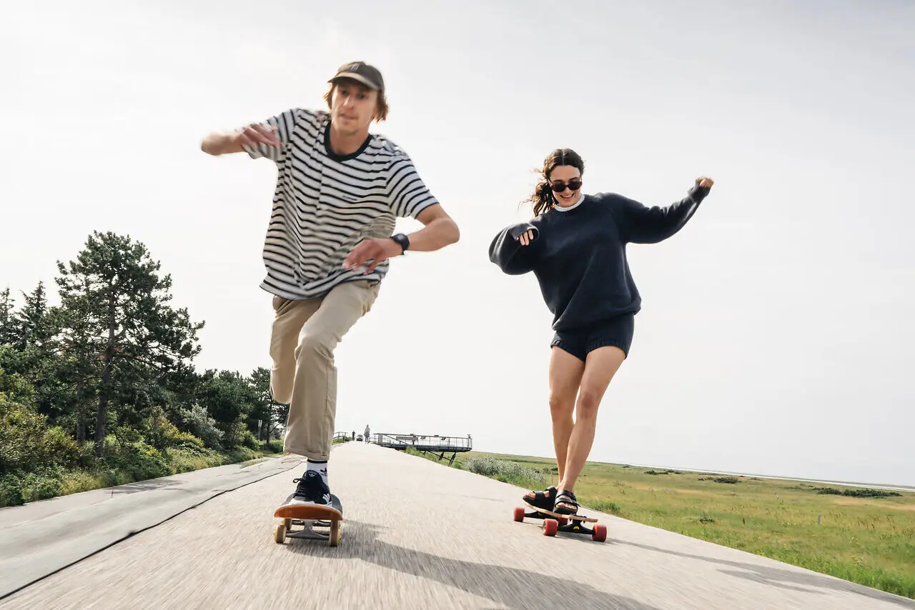 Zwei Menschen fahren auf Longboards über Asphalt.