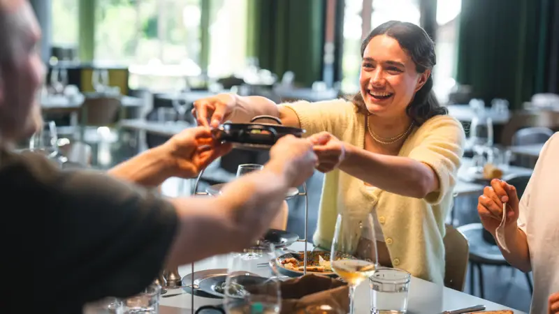 Several people are sitting at a table and passing food around to share.