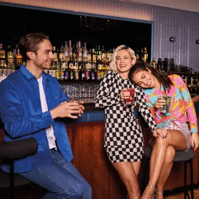 Drei junge Erwachsene genießen bunte Cocktails an einer stilvollen Hotelbar