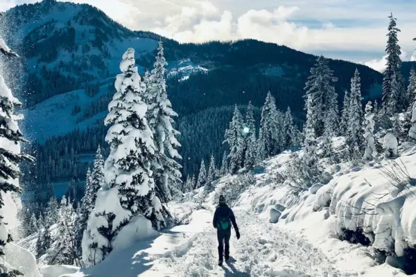 Eine Person geht auf einem verschneiten Pfad durch verschneite Berge.