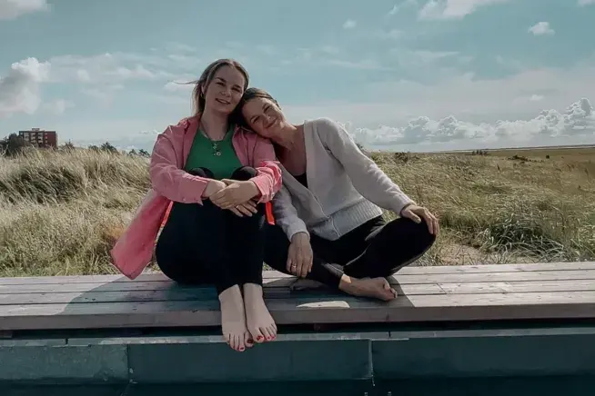 Yoga Retreat St. Peter-Ording with Mia and Johanna Yoga teachers Mia and Johanna are sitting on a bench outdoors under a cloudy sky.