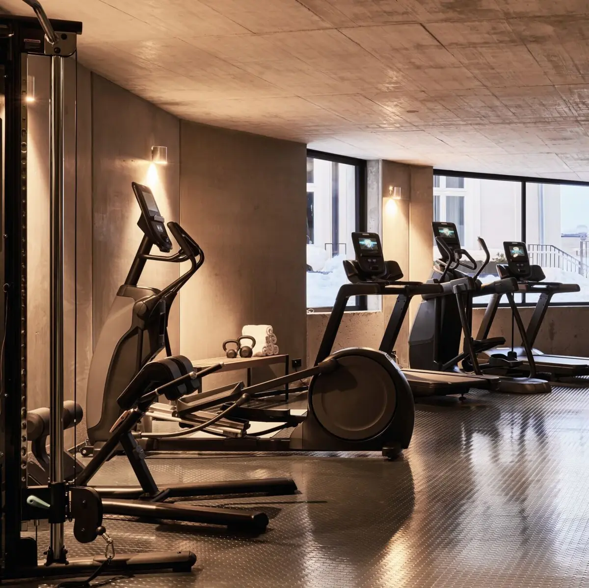 Modern fitness room with cross trainer, treadmills and power station in elegant concrete design and natural light