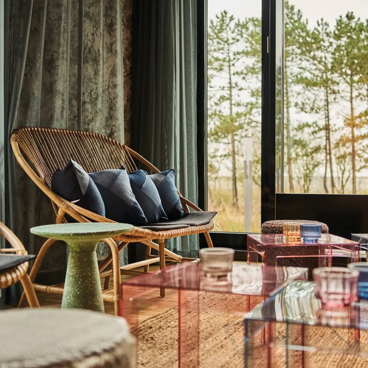 A seating area with multiple seating options, stools, and small tables in front of a large window overlooking greenery.